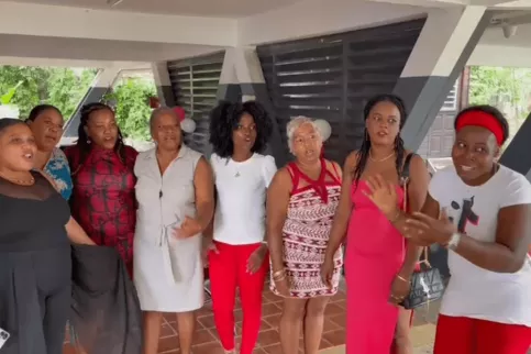 Neuf femmes debout, habillées pour une fête, souriantes et réunies sous un préau décoré de ballons, à l’occasion des fêtes de fin d’année dans les Maisons des Familles."