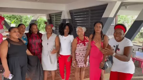 Neuf femmes debout, habillées pour une fête, souriantes et réunies sous un préau décoré de ballons, à l’occasion des fêtes de fin d’année dans les Maisons des Familles."